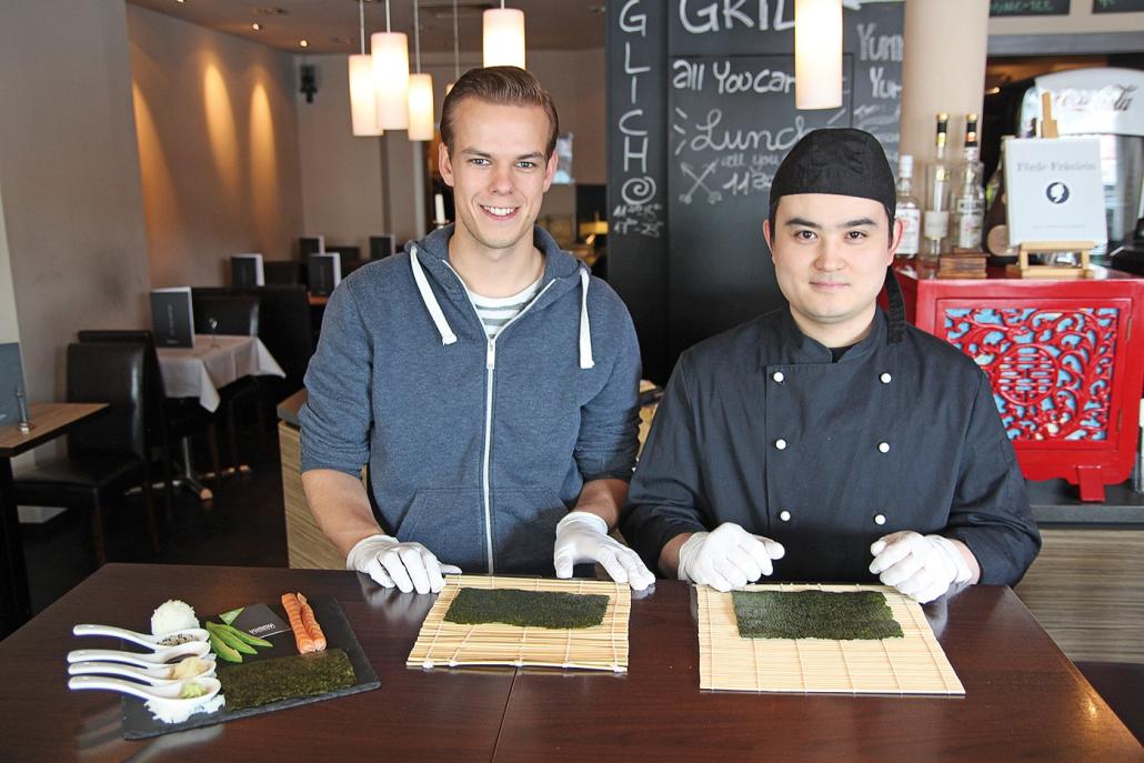 Wang und Jan (li.) haben die Zutaten bereitgelegt: Nori-Blätter, Sushireis, Lachsstreifen, Avocado, Sesam, dazu Sojasauce, Ingwer und Wasabi