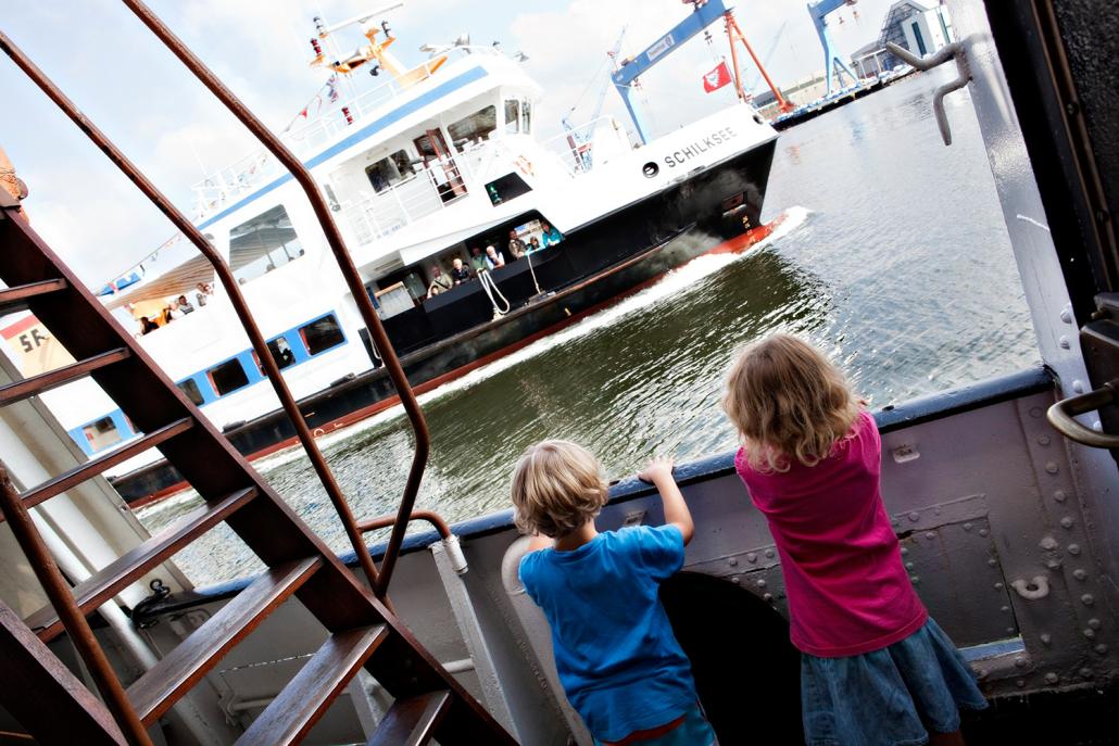 Zwei Kinder beobachten gespannt das Schiff, welches gerade an ihnen vorbeifährt