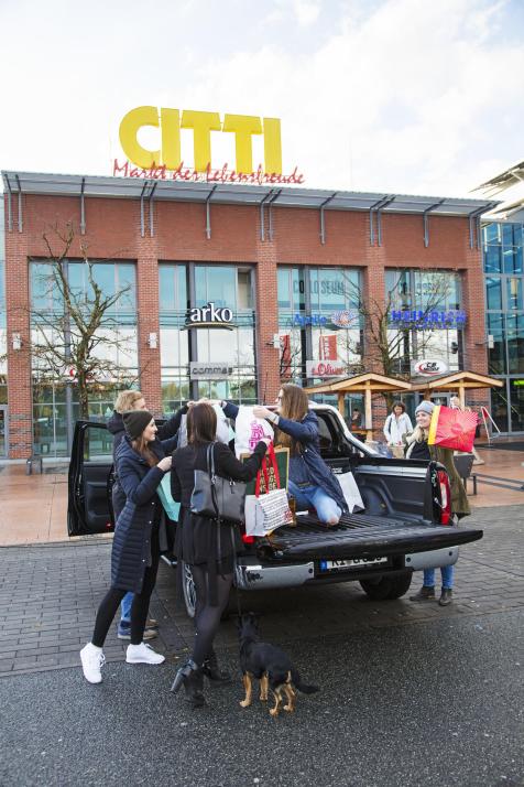 Am Parkplatz angekommen, müssen aber zunächst die Geschenke verstaut werden. Lisa hüpft auf die große Lade fläche, um die vielen Einkaufstüten ihrer Kollegen entgegenzunehmen