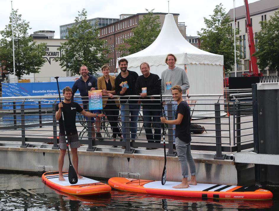 Die Organisatoren: Johannes Hesse (Kiel-Marketing), Nici Grenz (Deichperle), Nicolas Grimm (Programmleitung), Rainer Pasternak (Kulturreferent LH Kiel), Felix Pape (Alte Mu Impuls-W Kiel, v.l.), auf den SUPs Moritz Krusenbaum (Surf Shop Kiel), Frieder Ehlers (Ocean Global) 