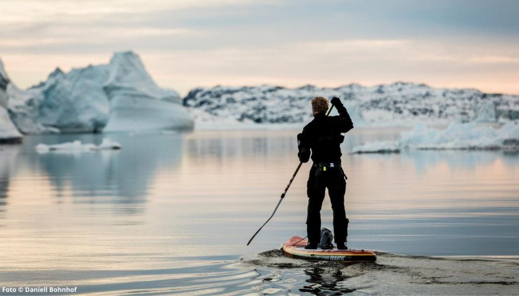 Michael Walther mit seinem SUP zwischen Eisbergen vor Grönland. Ohne den Klimawandel würde er nicht dort durch fahren können. Die Eisberge wären noch in ihrer vollen Größe erhalten und würden den Weg versperren
