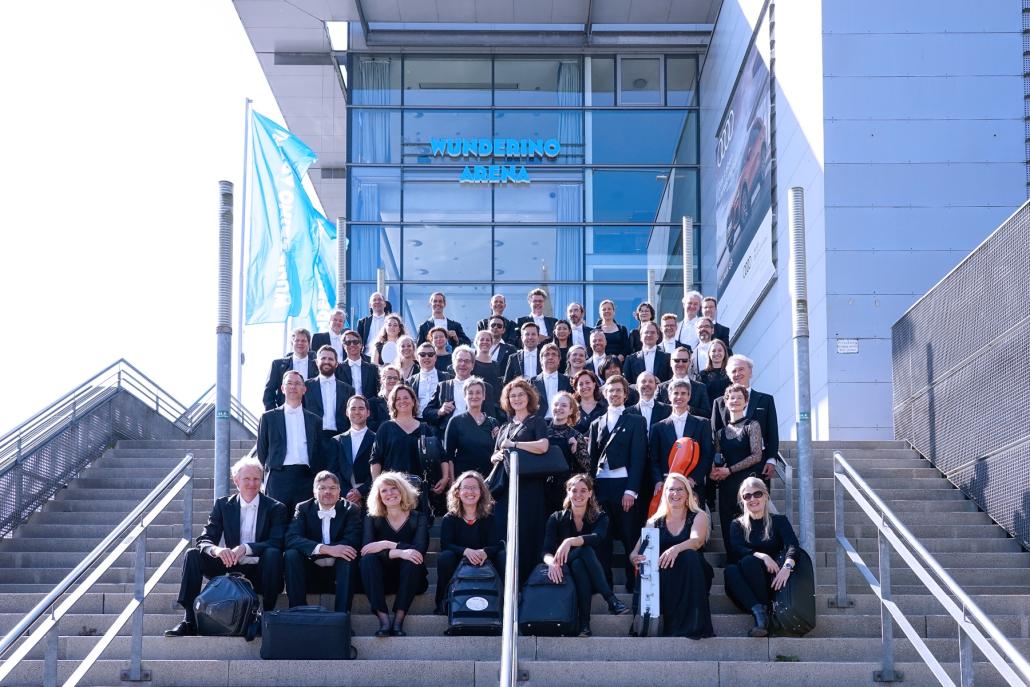 Das Philharmonische Orchester Kiel vor dem Eingang zur übergangsweisen Spielstätte: Aktuell finden die Konzerte statt im Kieler Schloss in der Wunderino Arena statt.