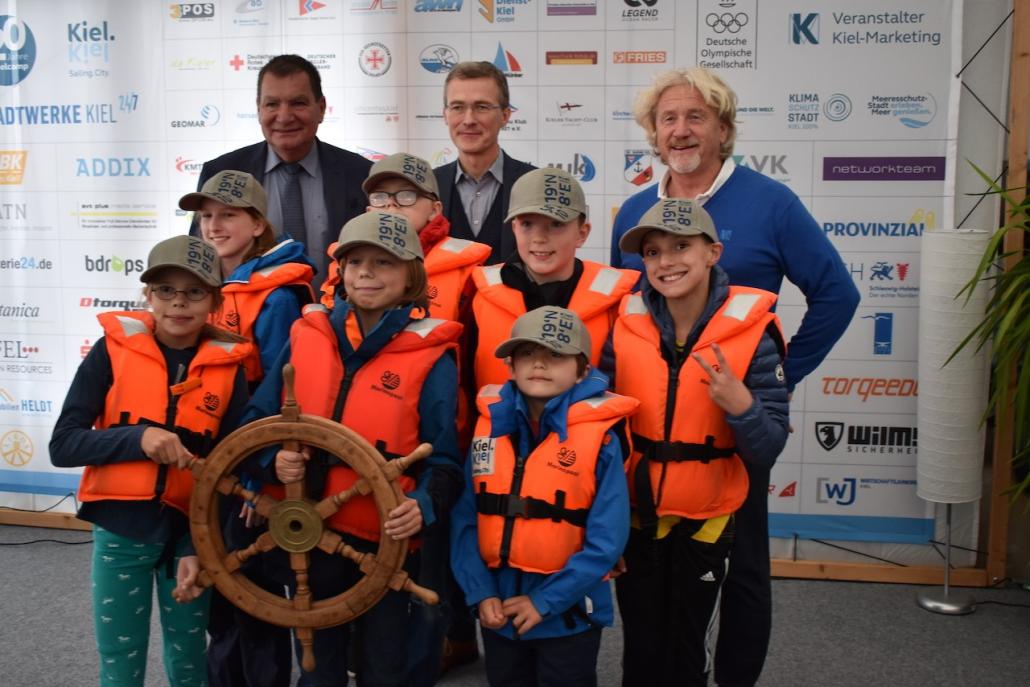 Gerwin Stöcken, Sportdezernent, Frank Meier, Vorstandsvorsitzender der Stadtwerke Kiel AG, und Uwe Wanger, Geschäftsführer von Kiel-Marketing, bei der traditionellen Übergabe des Steuerrads zum Saisonende an die Kinder.