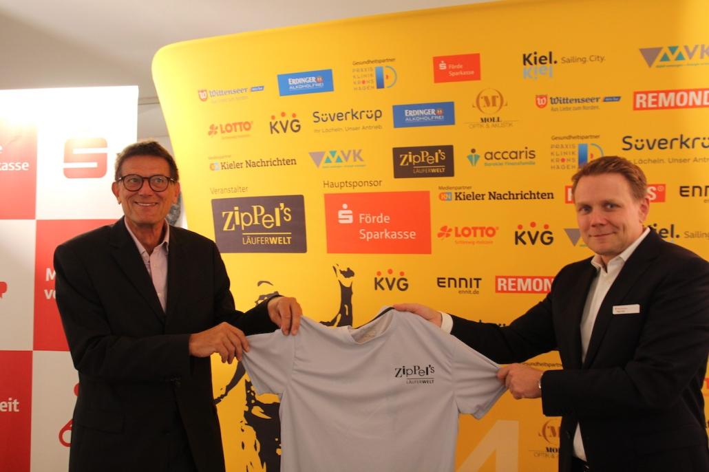 Rainer Ziplinsky (li.) präsentiert gemeinsam mit Peter Moll, stellvertetender Vorstandsvorsitzender der Förde Sparkasse, das neue Shirt zum Kiel.Lauf 2022.