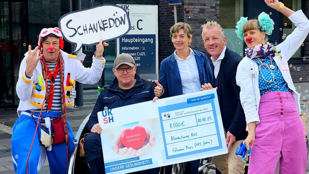Dr. med. Wurst (Chef-Klinikclown am UKSH, Campus Kiel, v.l.), Hans-Uwe Pries (Inhaber Glaserei Pries), Doris Pries, Pit Horst (Geschäftsführer des UKSH Freunde- und Fördervereins) und Dr. Tüdelüt (Klinikclown am UKSH, Campus Kiel) freuen...