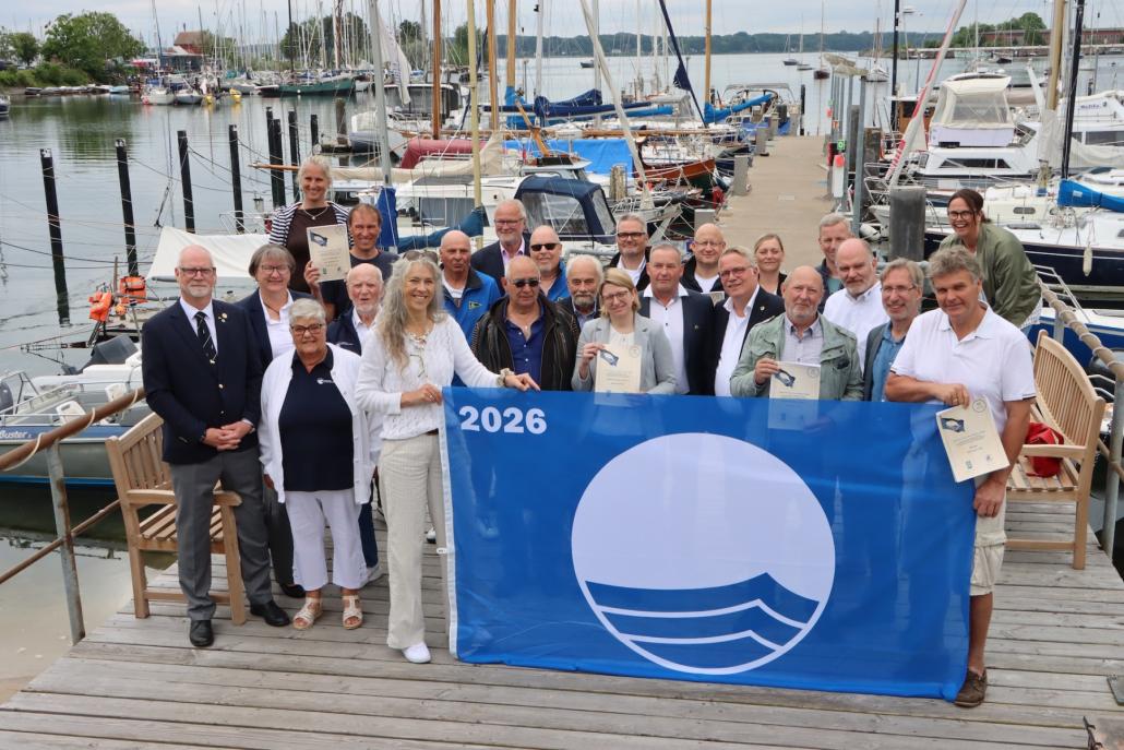 Stolz trotz unruhiger Zeiten: Stephanie Rieckhof-Sothmann und ihr Mann Frank Sothmann nehmen die Blaue Flagge 2026 im Plüschowhafen entgegen. 